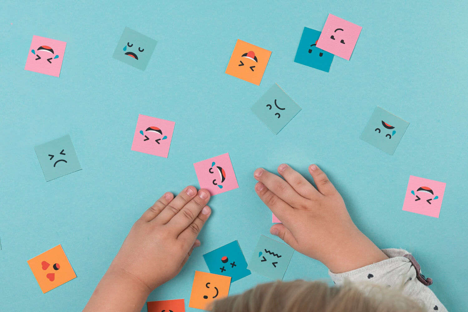 Kolorowe karteczki z różnymi minami, rączki dziecka – emocje dzieci w wieku przedszkolnym