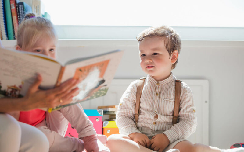 Adaptacja w przedszkolu. Chłopiec i dziewczynka oglądają książeczkę, którą pokazuje pani w przedszkolu